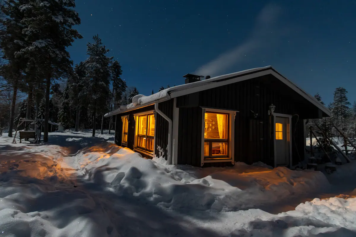 The Kentura guesthouse glowing warmly in the dark polar night, with soft light coming from inside, creating a cozy and inviting atmosphere.